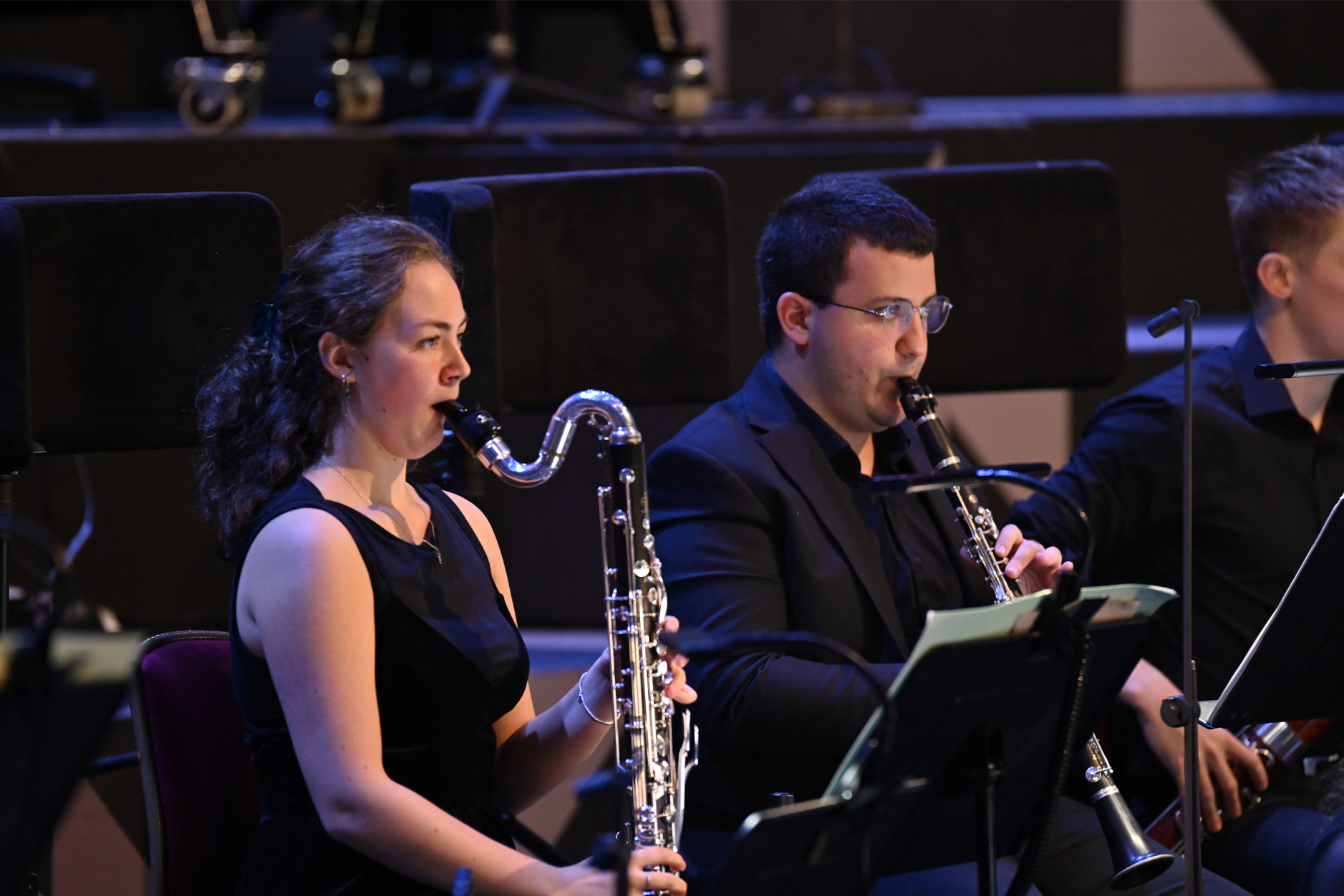 A female clarinettist performing in an orchestra, wearing smart black attire.
